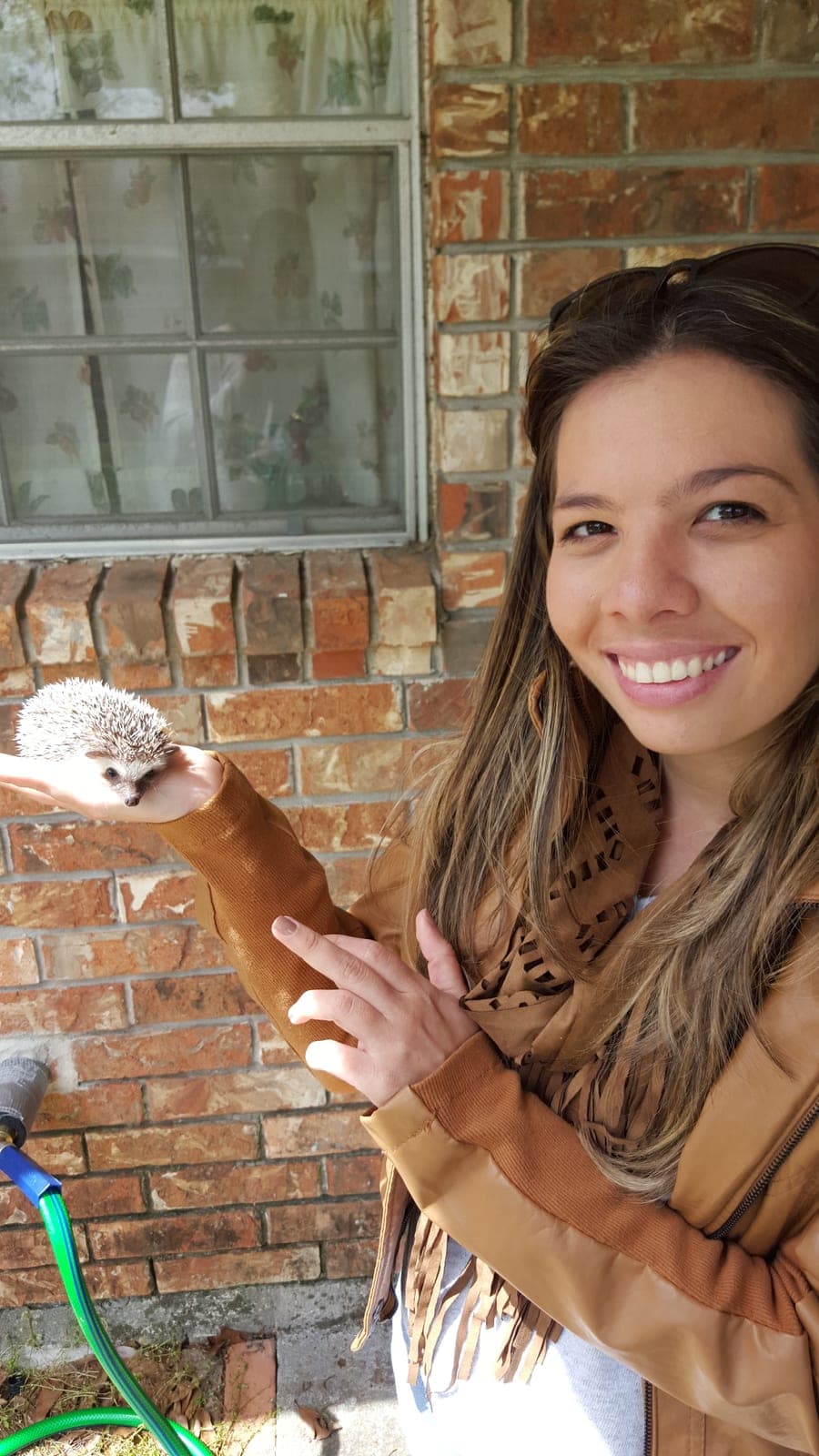 Silvana in a tan fringe jacket smiling beside a hedgehog balanced on her open hand.
