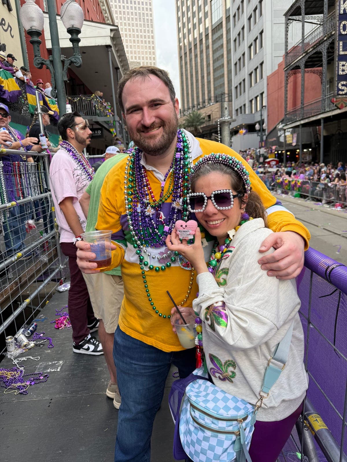 Silvana in pearl heart sunglasses layered in Mardi Gras beads, leaning back against Shaun on the parade route.